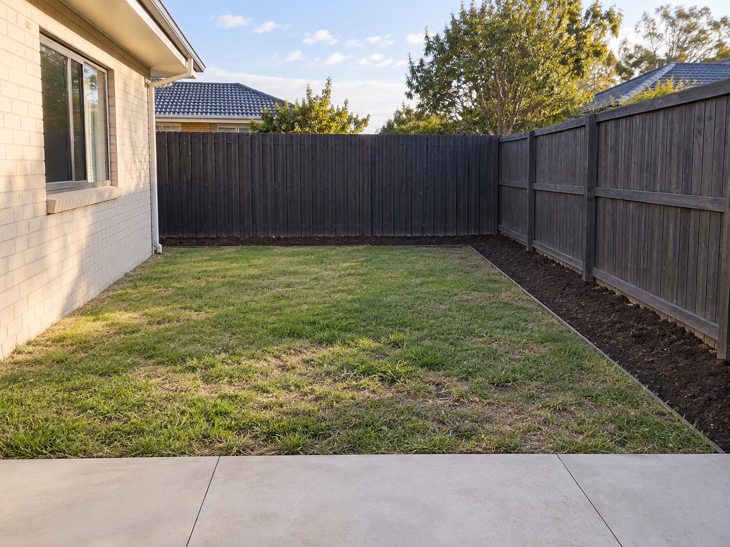 Example backyard before landscaping, with patchy grass and an empty garden bed